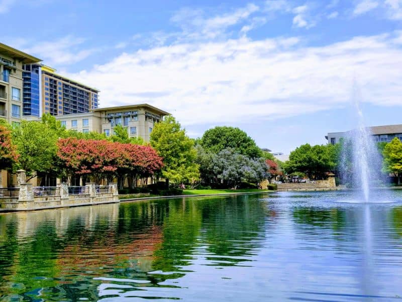 Scenic urban park in Plano, Texas with waterfront views, trees, and surrounding commercial buildings