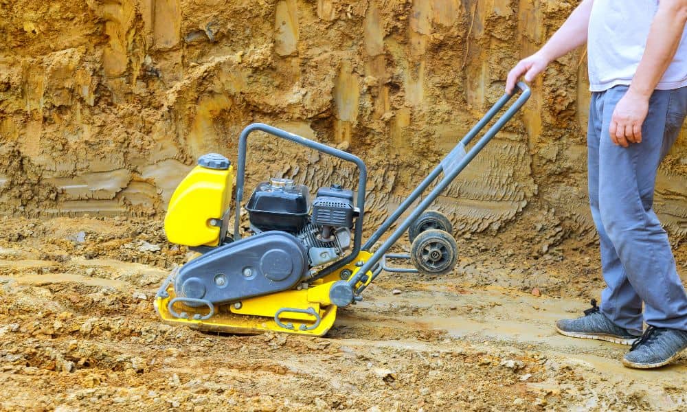 Worker using soil compaction equipment during site preparation for Proctor compaction testing